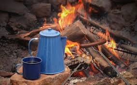 A blue enamel percolator pot and a matching mug are set against the backdrop of a crackling campfire, epitomizing the essence of outdoor coffee brewing. As flames gently lick the air, the sturdy percolator stands on a log, ready to infuse the grounds with the smoky essence of nature. This scene captures the quintessential outdoor coffee experience, where the simplicity of brewing with a percolator enhances the enjoyment of coffee in the great outdoors, complemented by the serenity of the wilderness.