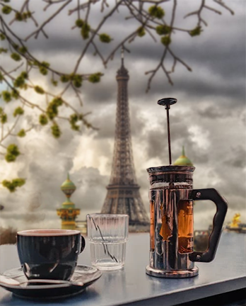 A French press coffee maker and cup set against a dramatic Paris backdrop with the Eiffel Tower, reflecting the rich history and international roots of the French press brewing method