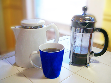 A Sowden SoftBrew coffee pot next to a French press and a vibrant blue mug of coffee on a tiled countertop, showcasing different brewing methods.
