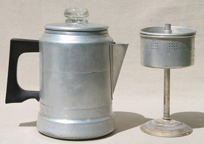 A vintage aluminum stovetop coffee percolator alongside its separate filter basket is displayed against a neutral background. The percolator's worn surface and the basket's perforated design highlight the simplicity and efficiency of traditional coffee brewing methods, distinguishing it from modern drip coffee makers. This image showcases the essential parts of the percolator where water transforms into steam, rises through the grounds, and brews into rich, flavorful coffee through a process that enriches the coffee's bold taste with each cycle.