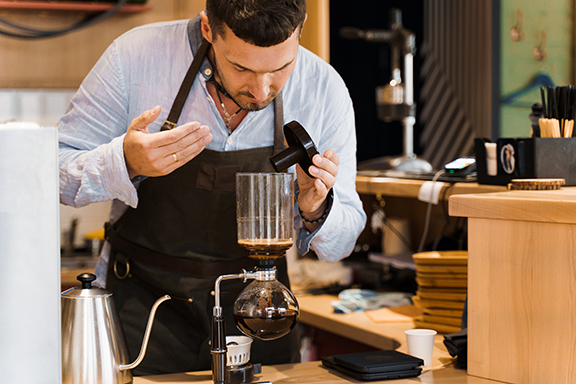 A focused barista in an apron carefully setting up a vacuum siphon coffee maker, exemplifying the precision and expertise required in the siphon brewing process.