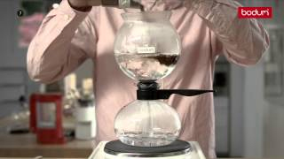 A person operating a Bodum siphon vacuum coffee maker, illustrating the hands-on approach that distinguishes siphon coffee brewing from other methods.