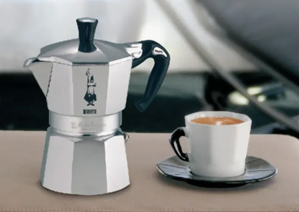 A Bialetti Moka Pot next to a cup of freshly brewed coffee, representing the rich taste of Italian Moka Pot coffee