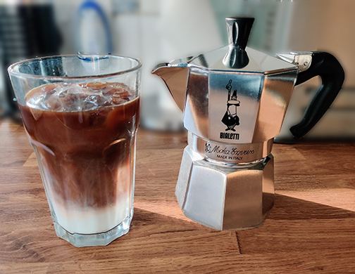 A Moka Pot next to a refreshing glass of iced latte, illustrating the simple pleasure of a homemade Moka Pot iced coffee, perfect for a warm day.