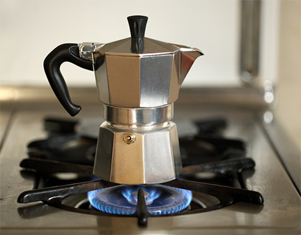A Moka Pot on a gas stove with a blue flame underneath, depicting the brewing process of making rich, authentic Italian coffee.